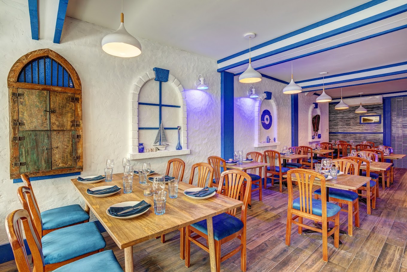 Salle à manger du Petit Souvlaki Grec : murs blancs, banquettes bleues et tables en bois