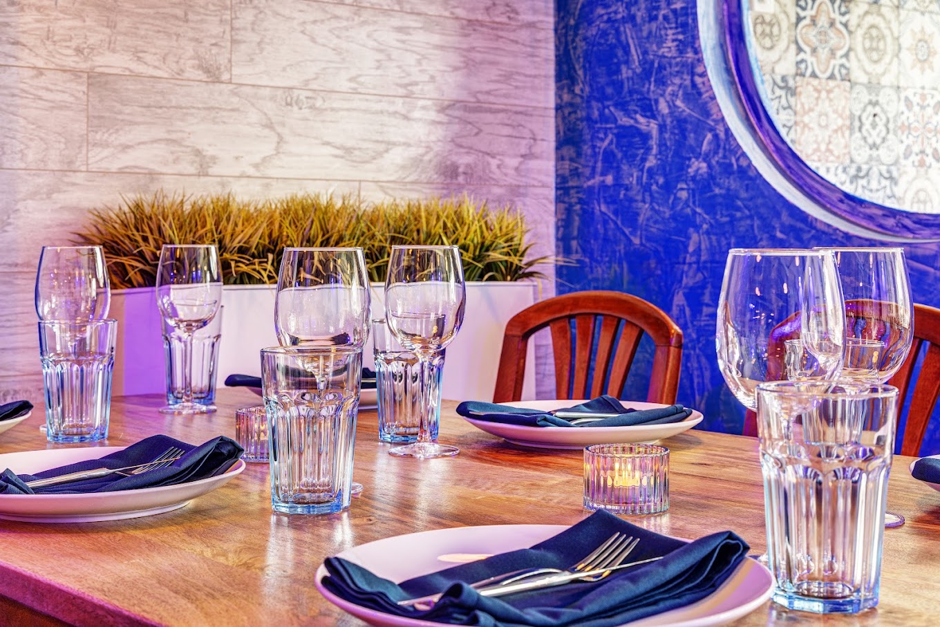 Table dressée au Petit Souvlaki Grec avec serviettes bleu marine, verres à vin et mur bleu